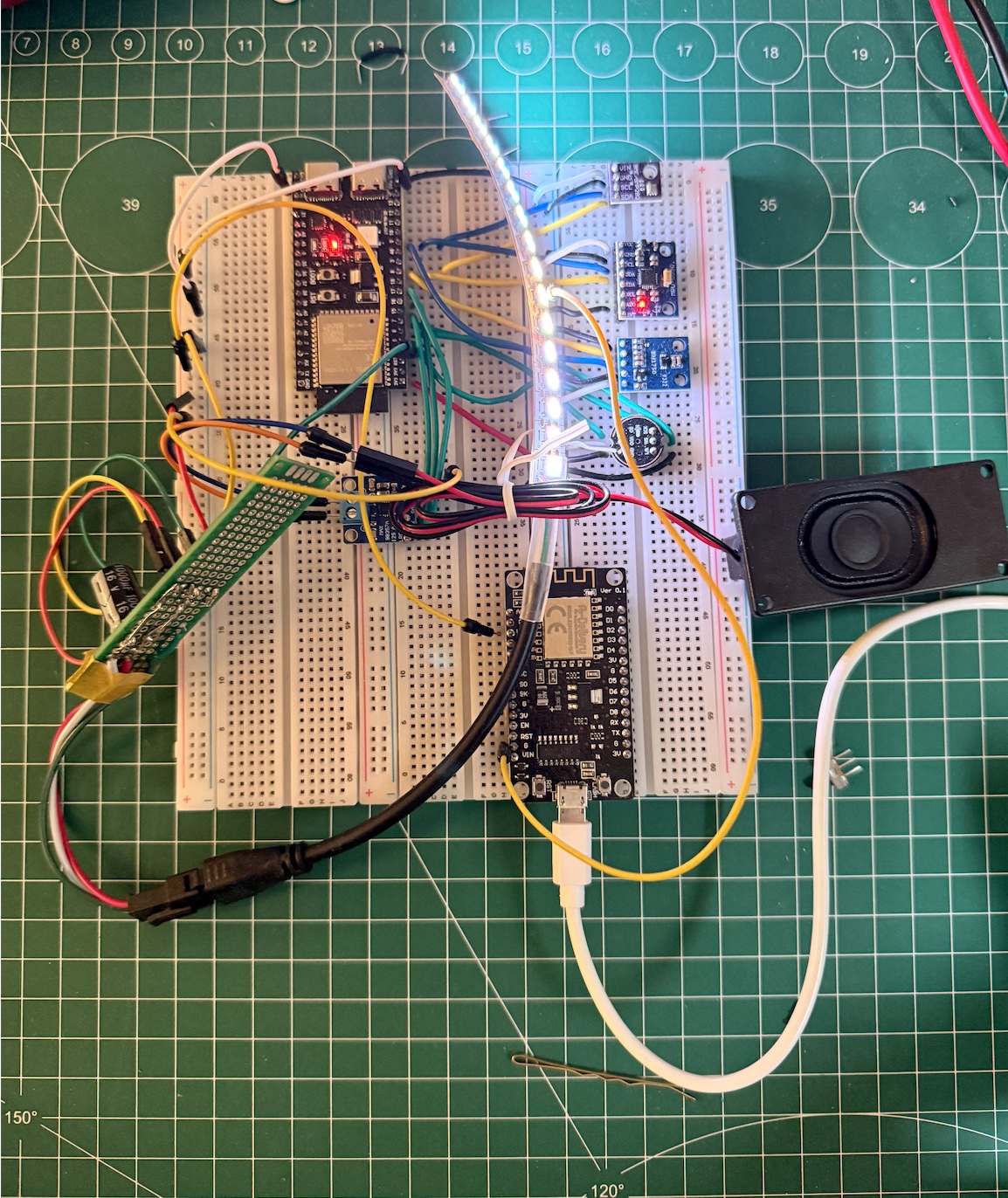 A fully wired Creature prototype on two breadboards, with sensor boards, an LED strip, a speaker, and two microcontrollers arranged on a green cutting mat.