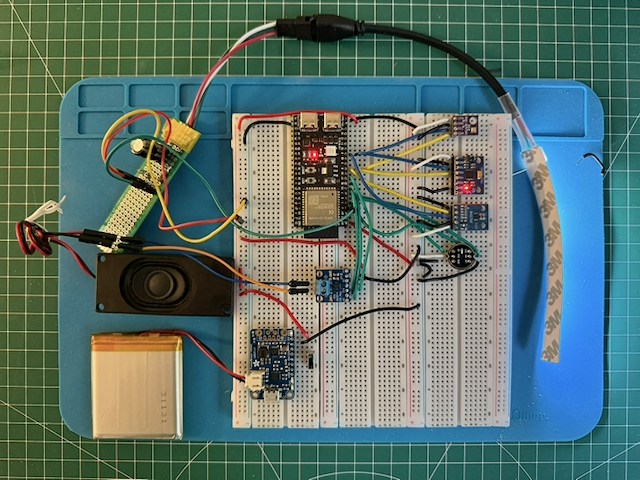 The current Creature prototype on a blue mat, with a battery, speaker, sensors, and wiring arranged around a breadboard.